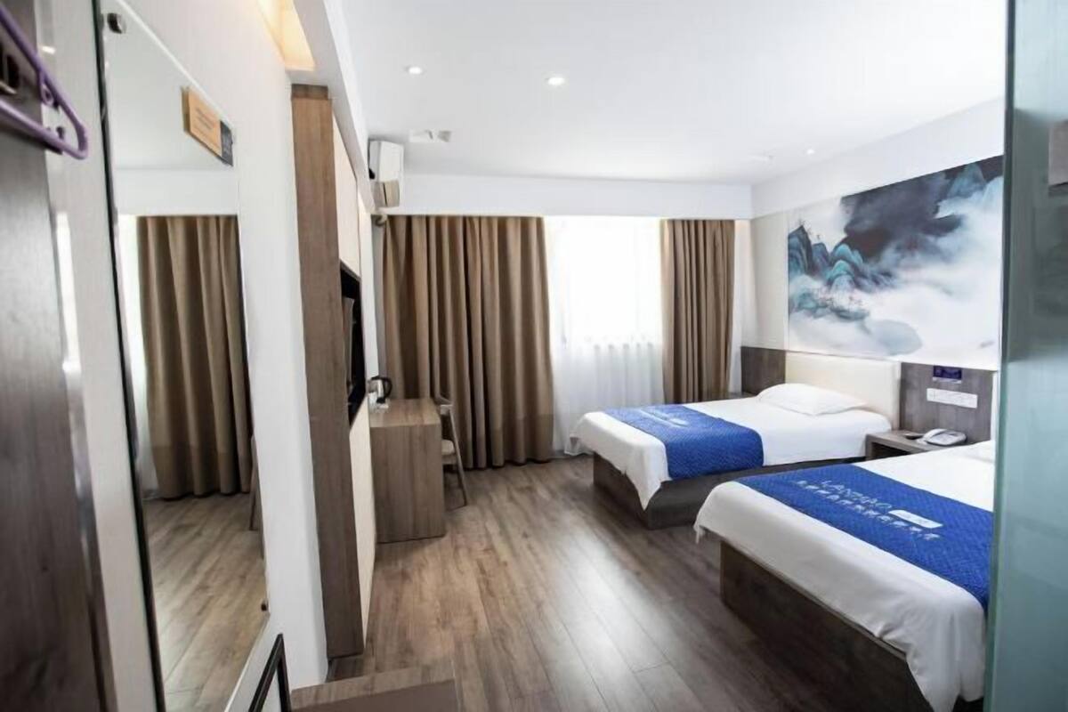 Ein Hotelzimmer mit zwei Betten, einem Schreibtisch, einem Stuhl, einem Fernseher und einem Bild an der Wand.