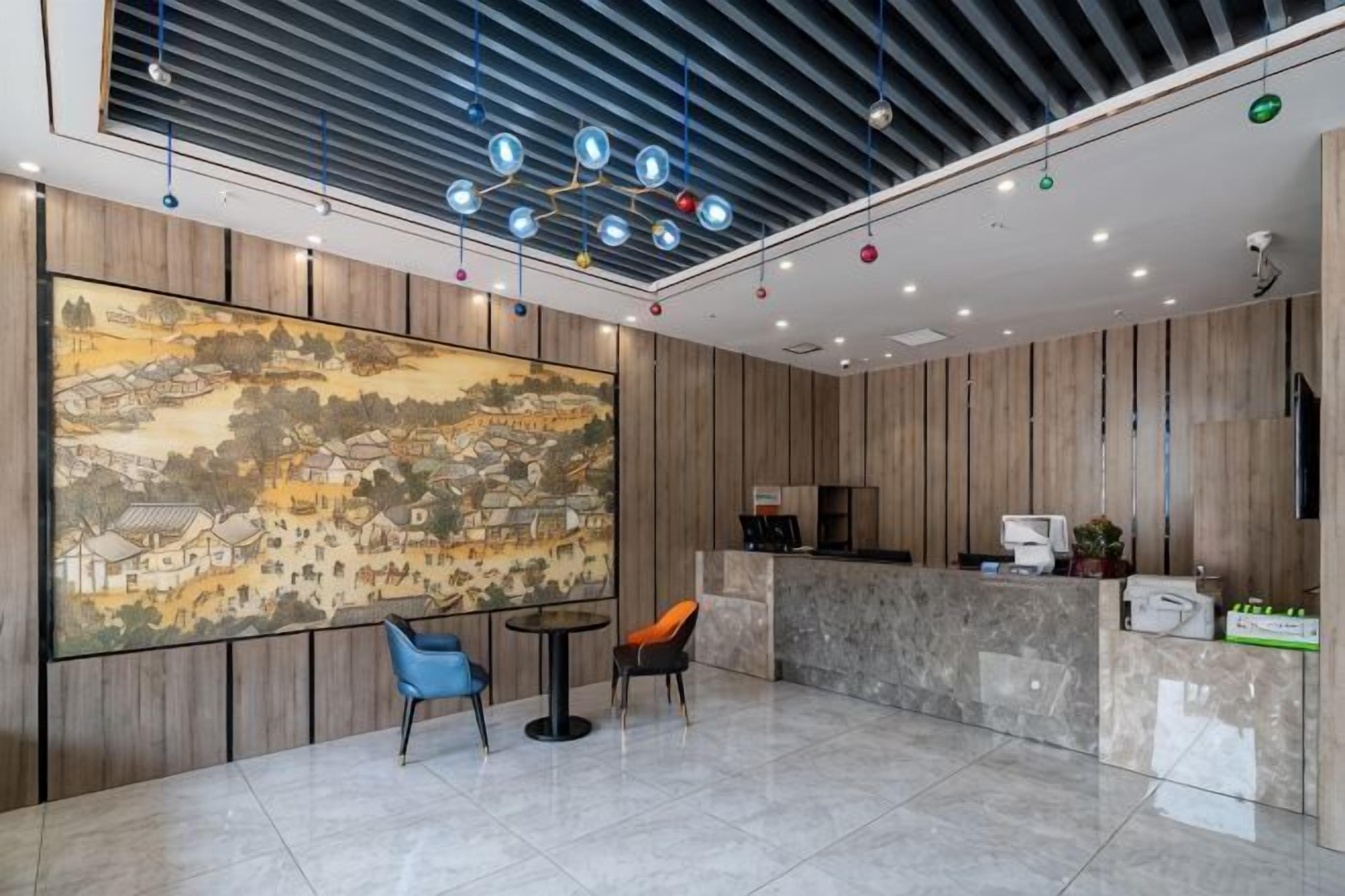 A lobby with a large mural, a reception desk, two chairs, and a modern ceiling design.