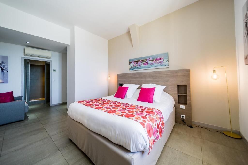A modern hotel room with a large bed, a sofa, and a painting on the wall.