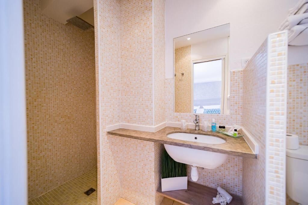 A bathroom with a tiled shower, a sink with a mirror, and a toilet.