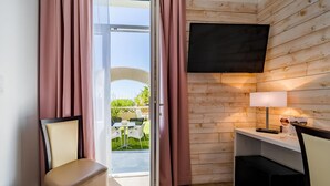 Una habitación con puerta de vidrio corredera, un televisor de pantalla plana montado en la pared, un escritorio pequeño con lámpara y una silla.