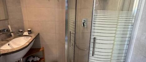 A modern bathroom with a curved glass shower enclosure, a sink with a marble countertop, and a toilet.