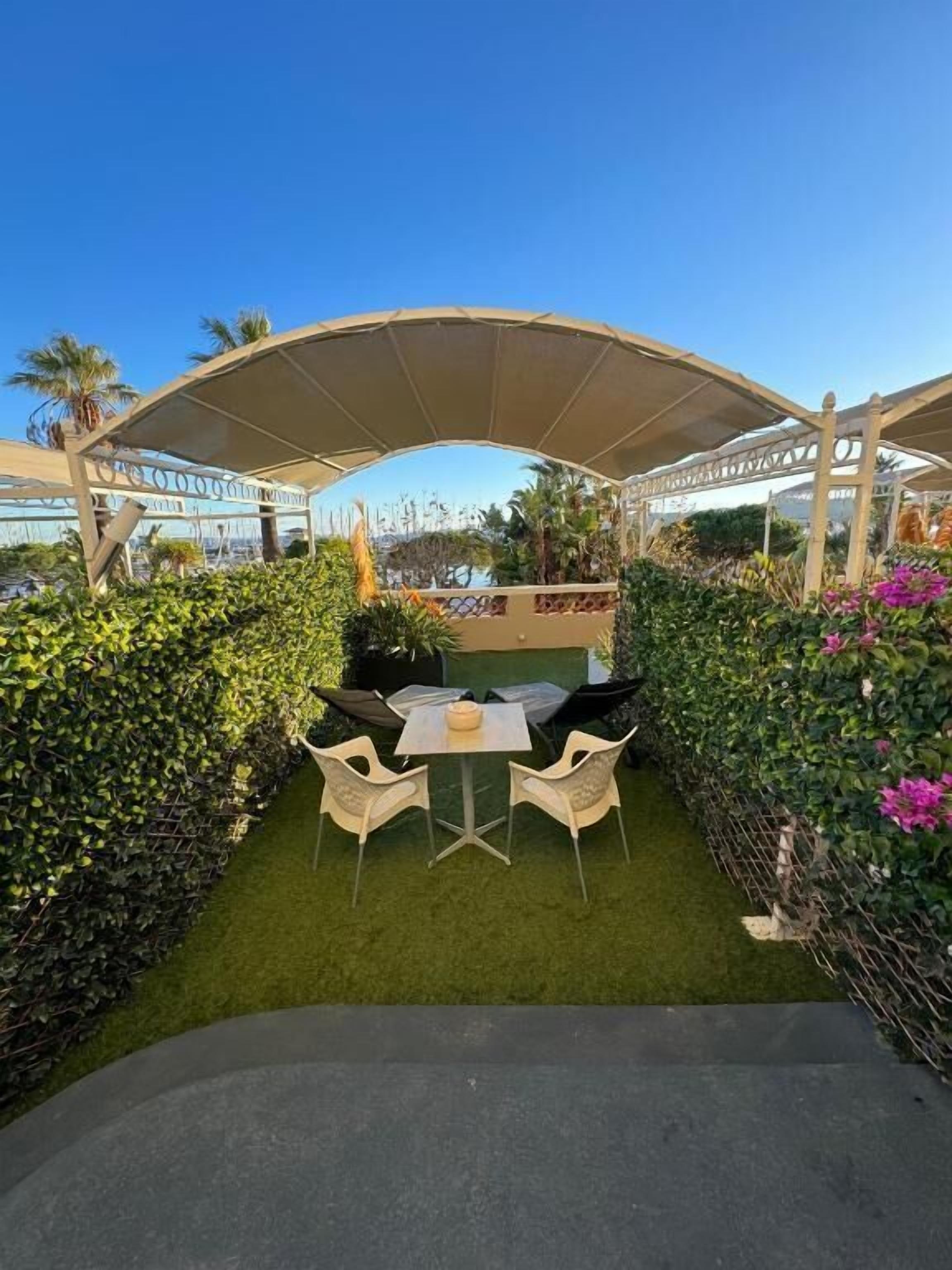 Un patio al aire libre con una mesa y sillas, rodeado de follaje y una estructura de pérgola.