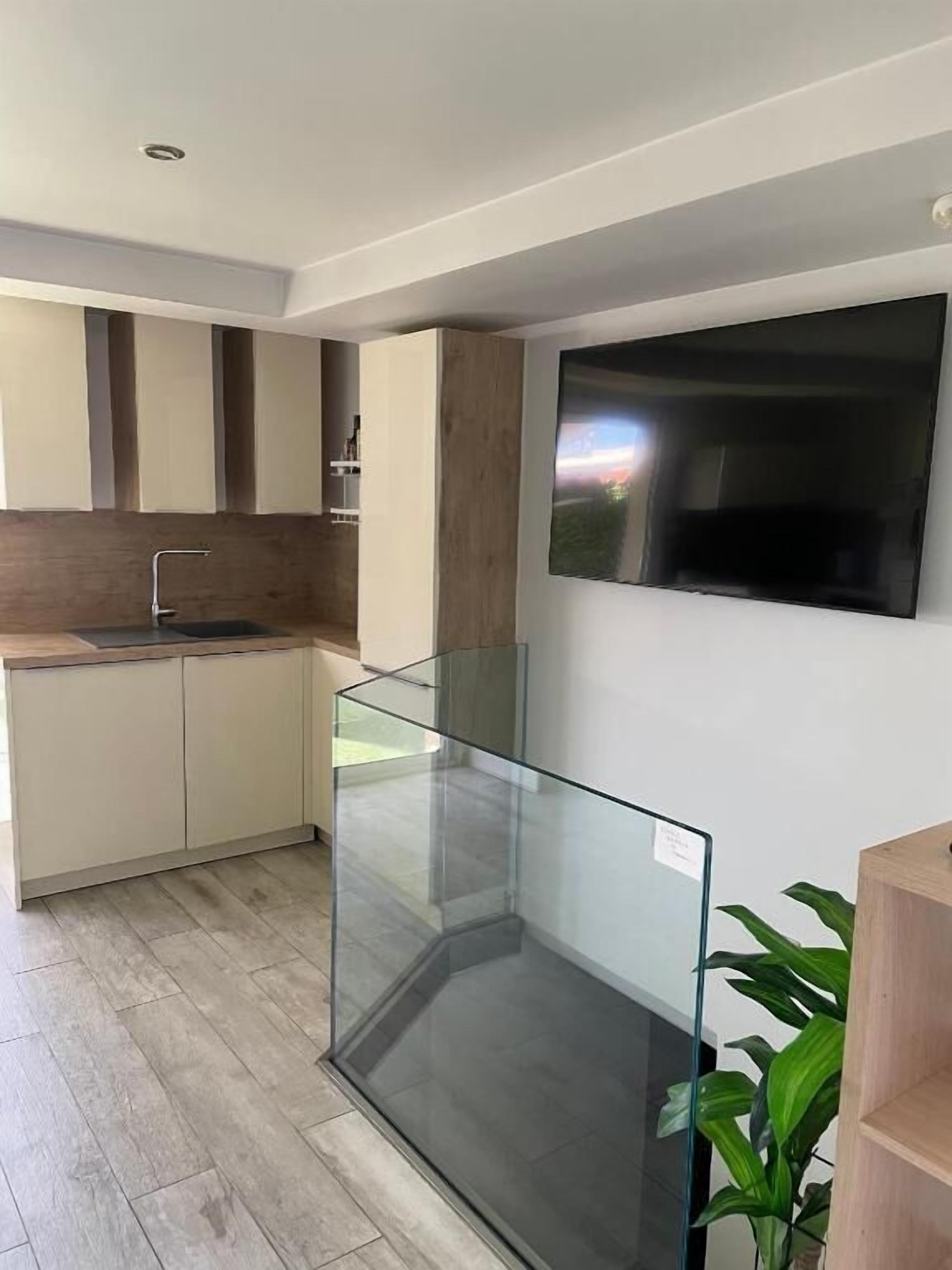Una cocina moderna con separador de vidrio, armarios de madera y televisor integrado.