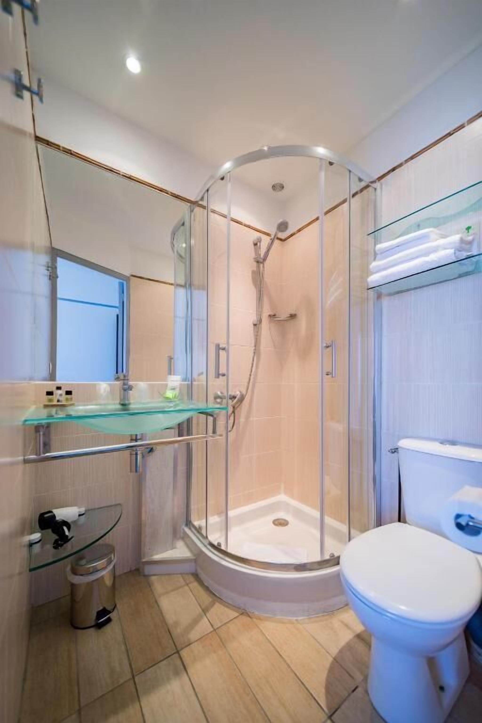 Une salle de bain moderne avec une douche à parois de verre, des toilettes et une étagère en verre où sont rangés les articles de toilette.