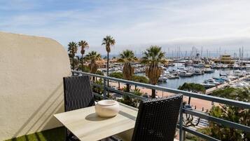A balcony with a table and chairs overlooking a marina with boats and palm trees.