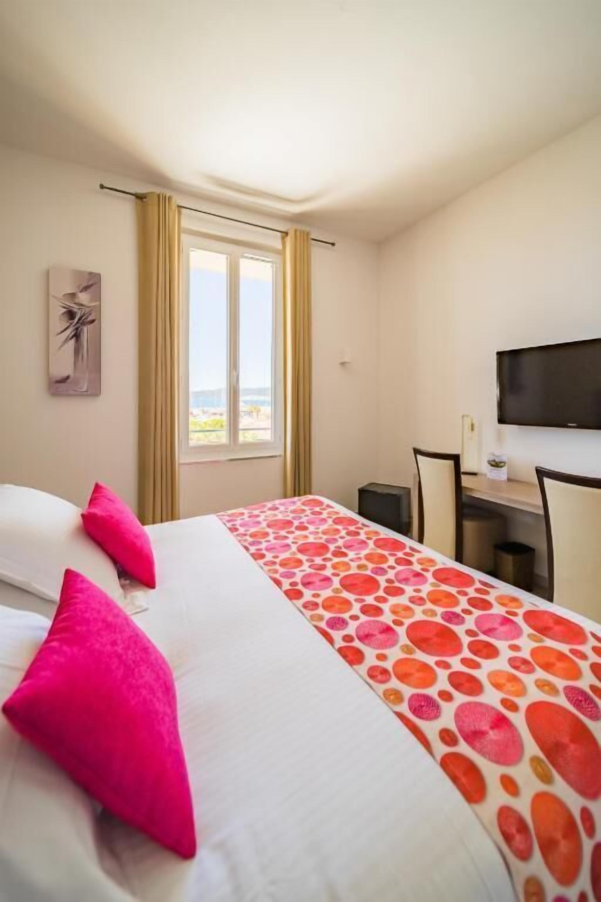 A hotel room with a bed, a desk, a chair, a television, and a window with curtains.