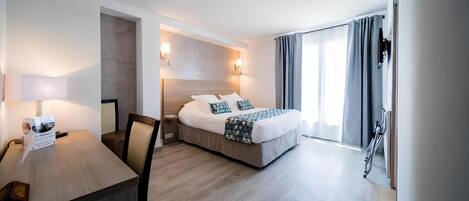 Ein modernes Hotelzimmer mit Bett, Schreibtisch und Stuhl. Ein Fenster mit Vorhängen bietet einen Ausblick nach draußen.