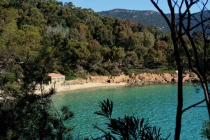 Un paisaje costero con playa, agua turquesa cristalina y un pequeño edificio de techo rojo.