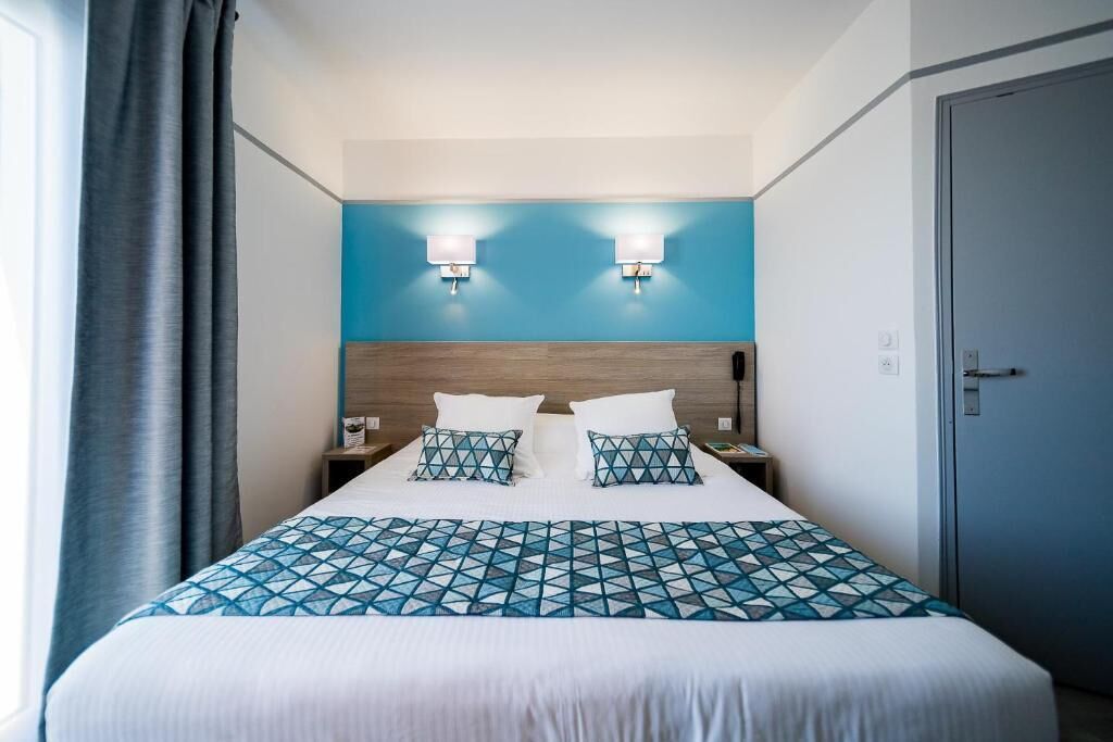 A hotel room with a large bed, two bedside lamps, a wooden headboard, and a blue accent wall.