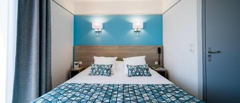 Une chambre d’hôtel avec un grand lit, deux lampes de chevet, une tête de lit en bois et un mur d’accent bleu.