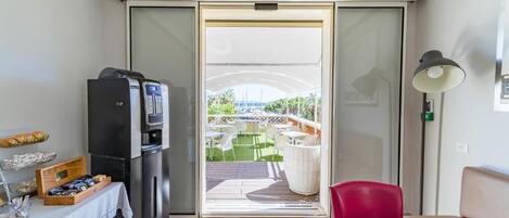 Une pièce de taille modeste dotée d’une porte-fenêtre coulissante qui donne sur une terrasse extérieure. On peut y voir un réfrigérateur noir et une petite table avec des collations.