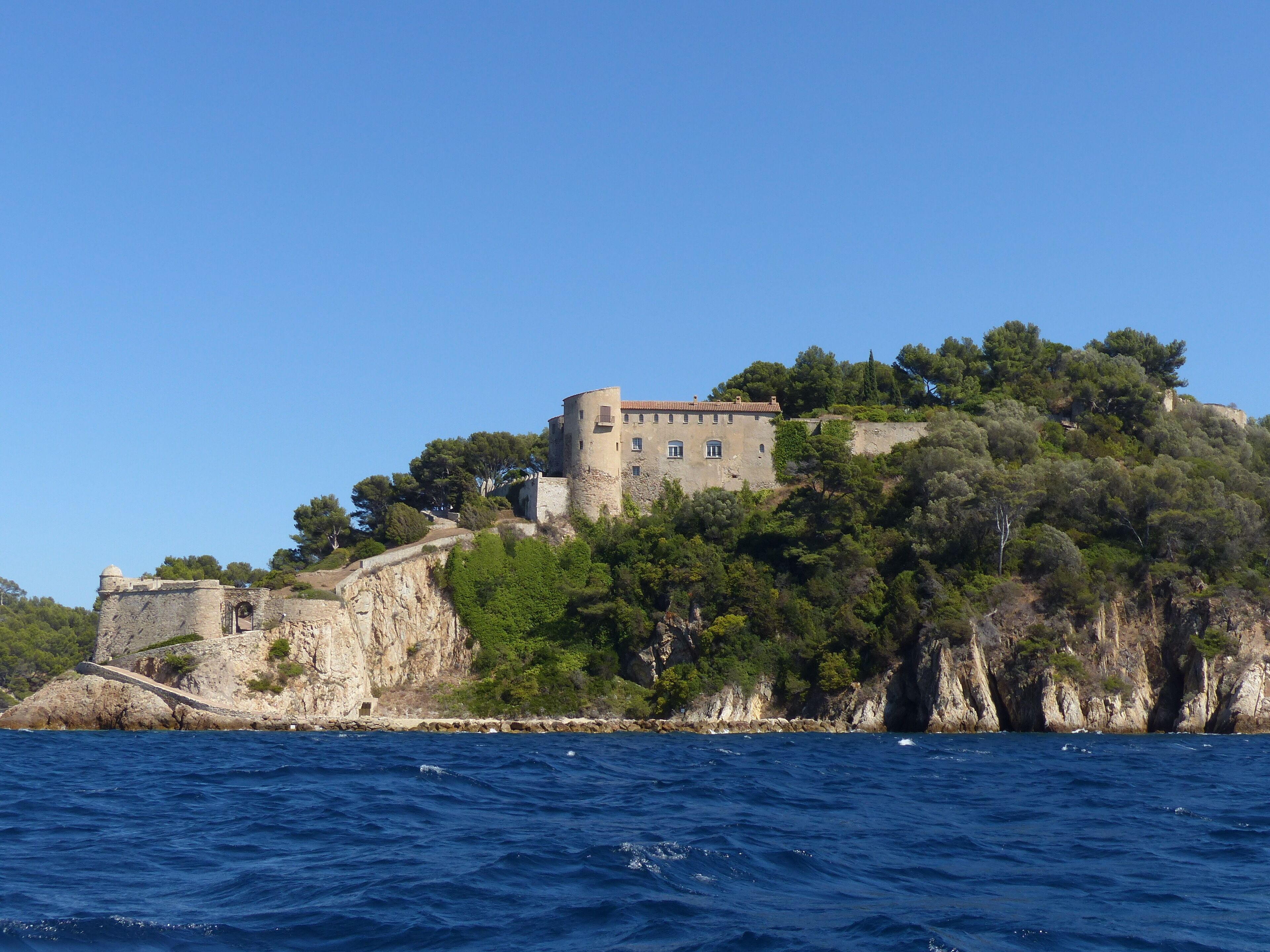 Un castillo costero con estructura fortificada, rodeado de abundante vegetación y vistas al mar.