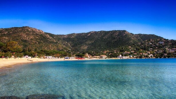 Una playa costera con aguas cristalinas, una orilla arenosa y montañas al fondo.
