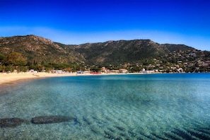 A coastal beach with clear waters, a sandy shore, and a mountainous backdrop. - Le Rabelais (Le Lavandou)