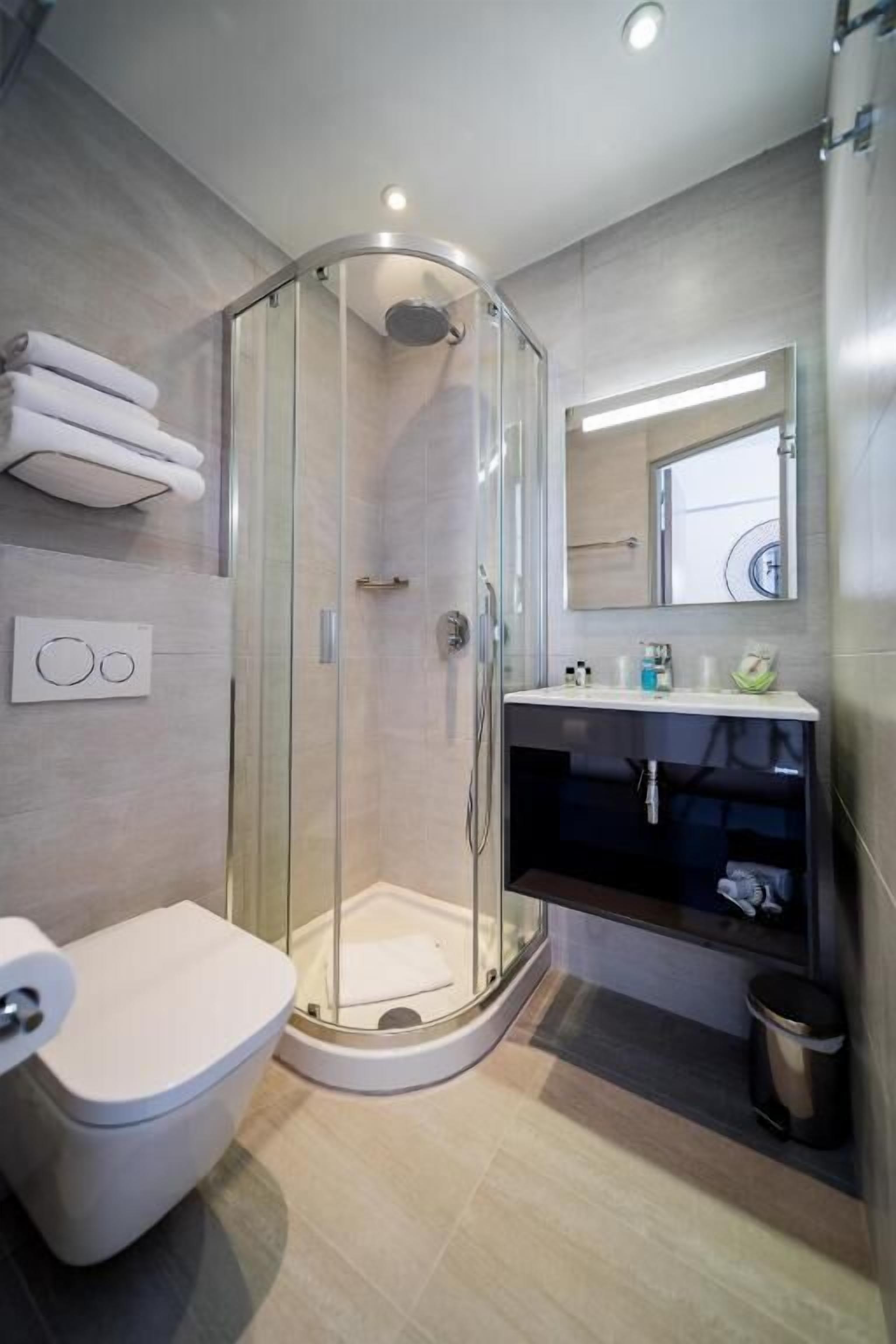 Een moderne badkamer met een douchecabine van glas, een toilet, een wastafel met spiegel erboven en een prullenbak.