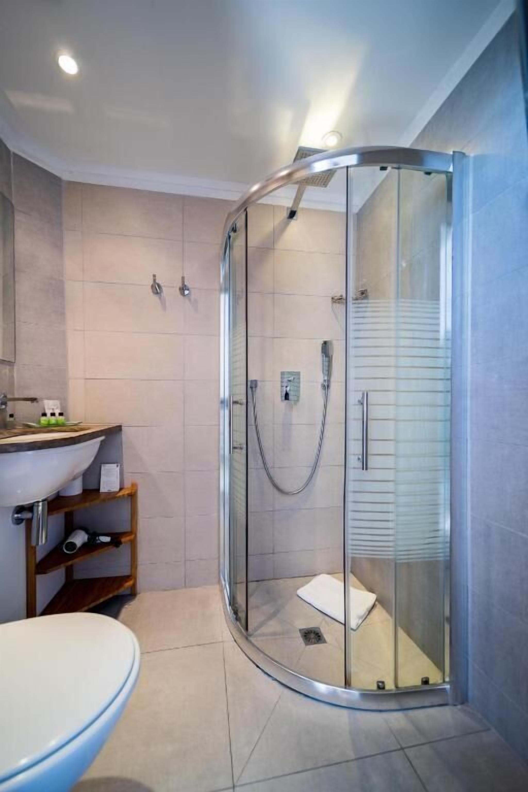 Une salle de bain moderne avec une douche à parois de verre, un lavabo blanc et une étagère en bois.