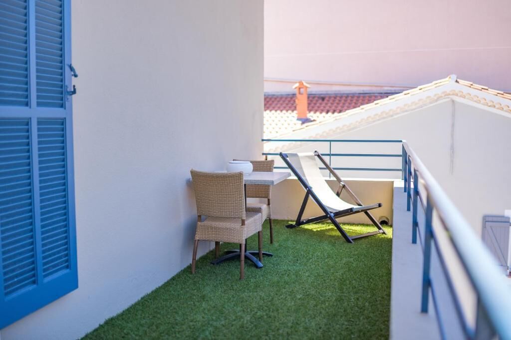 A balcony with artificial grass, a wicker chair, a small table, and a blue railing.