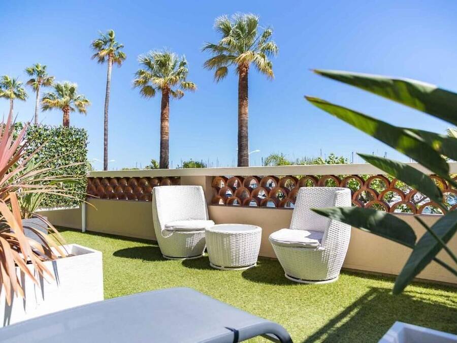 Une terrasse dotée de meubles en osier blanc, de palmiers et d’un mur décoratif.