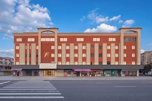 Un hotel de varios pisos con un llamativo logo con la letra 'F', una entrada central y un paso de peatones al frente.