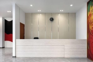 Zona de recepción con un mostrador de tonos claros, un reloj en la pared y una puerta a la izquierda.
