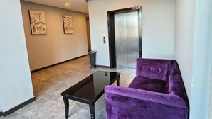 A hallway with a purple sofa, a glass coffee table, and an elevator. - Fanpo Hotel (Zhongshan)