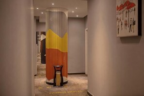 A hotel corridor with a tall pillar, a chair, and a painting on the wall.