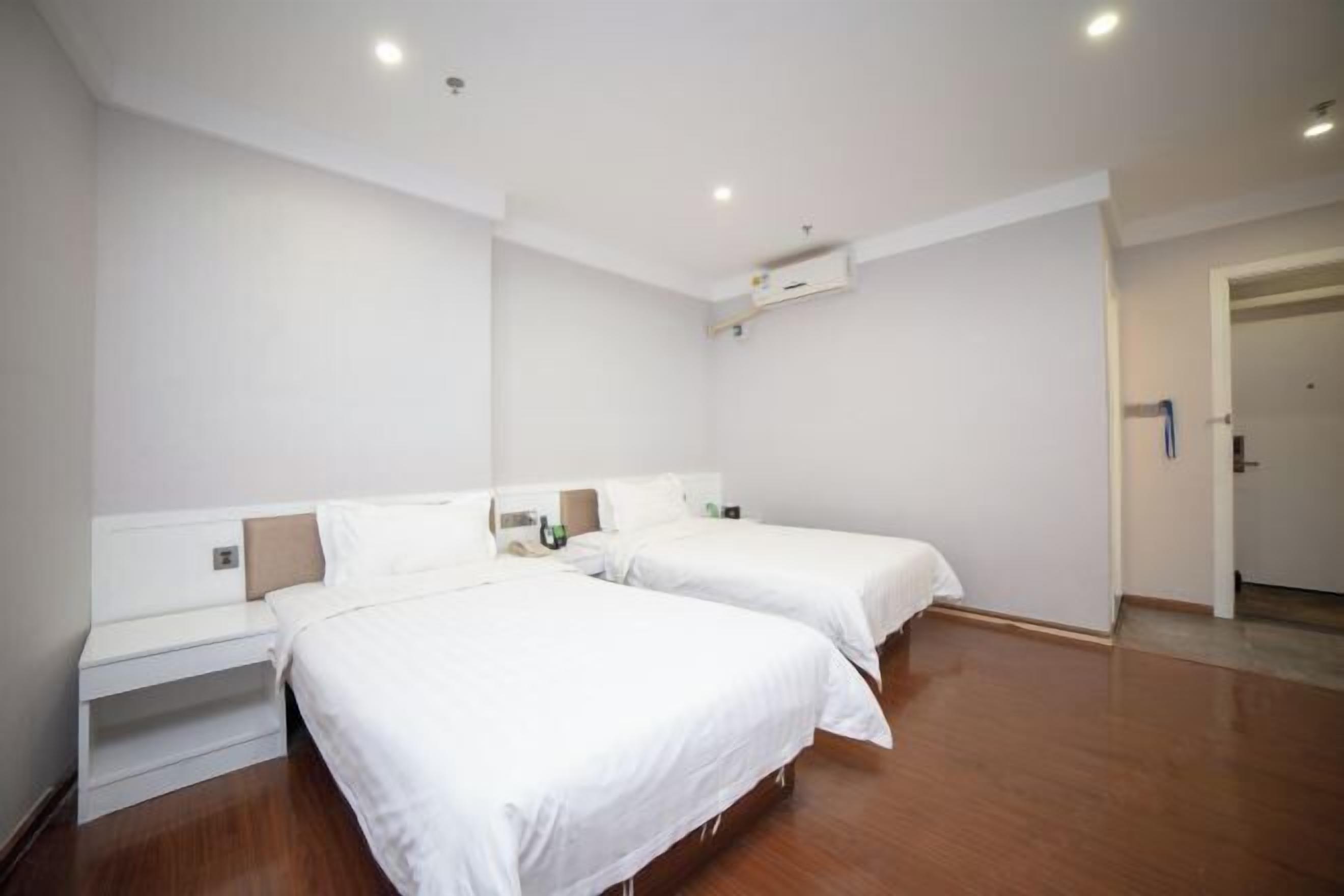 Une chambre d’hôtel avec deux lits, un mur blanc, un plancher en bois et une porte.