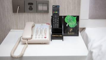 Habitación de hotel con una cama blanca, un teléfono blanco, un control remoto negro y un cartel de hotel verde.