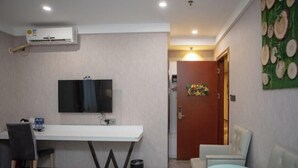 A hotel room with a flat-screen TV, a white desk, two chairs, a small trash bin, and a door with a decorative panel. - Fanpo Hotel (Zhongshan)