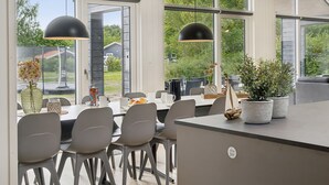 Un espace de salle à manger moderne, doté d’une grande table, de chaises et de luminaires suspendus.