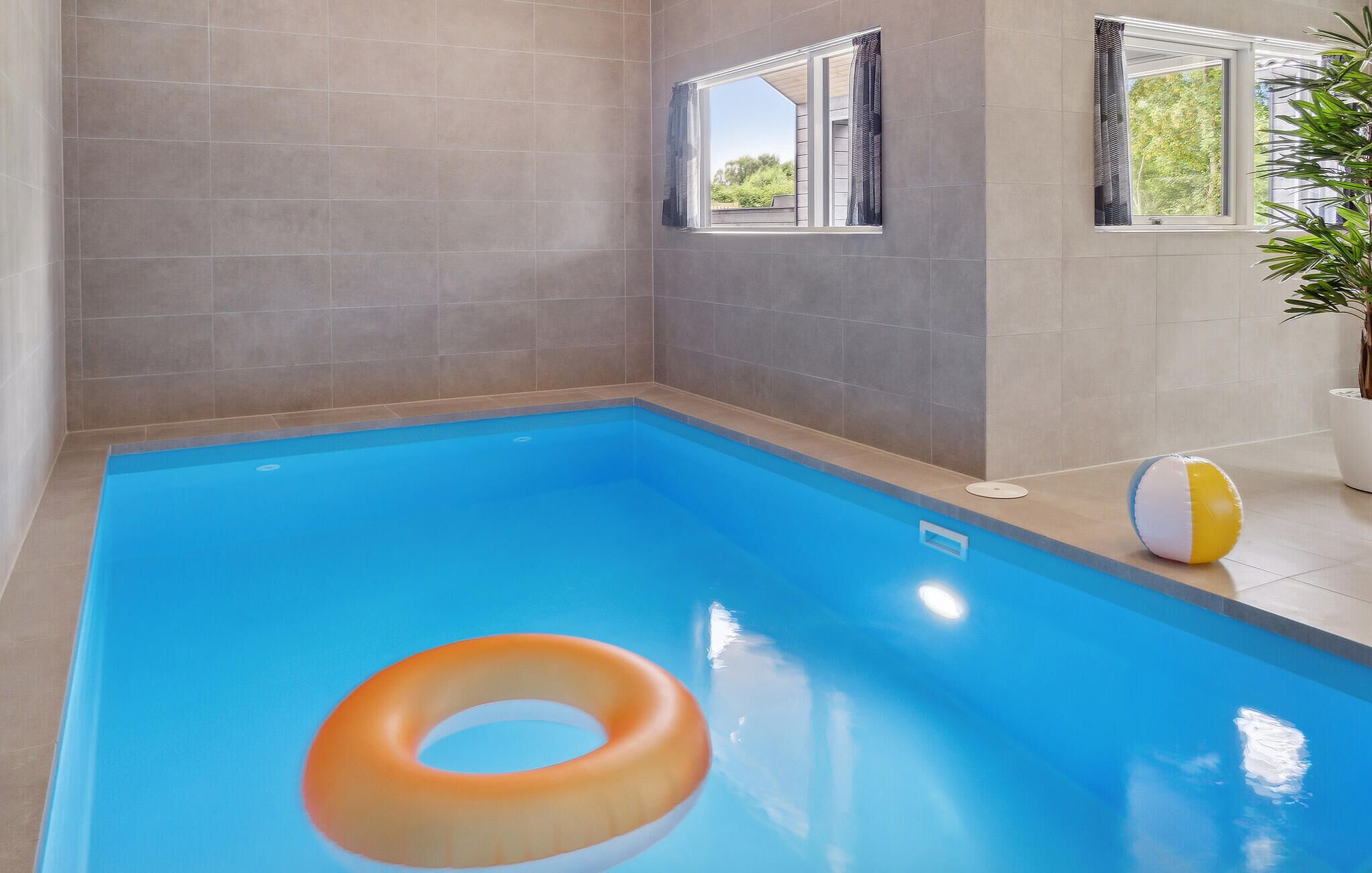 A swimming pool with a single inflatable ring, tiled walls, and windows with curtains.