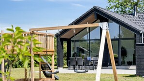 Une maison moderne dotée d’une grande baie vitrée, d’une balançoire en bois et d’un espace patio.