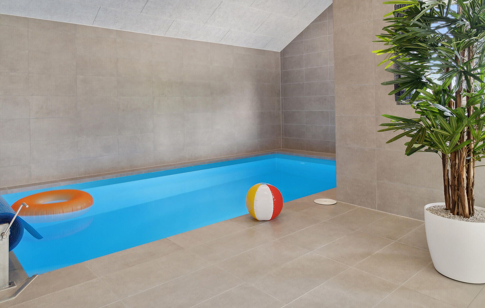 Ein Hallenbad mit blauer Wasseroberfläche, einem weißen und roten Strandball und einem orangefarbenen Schwimmreifen.