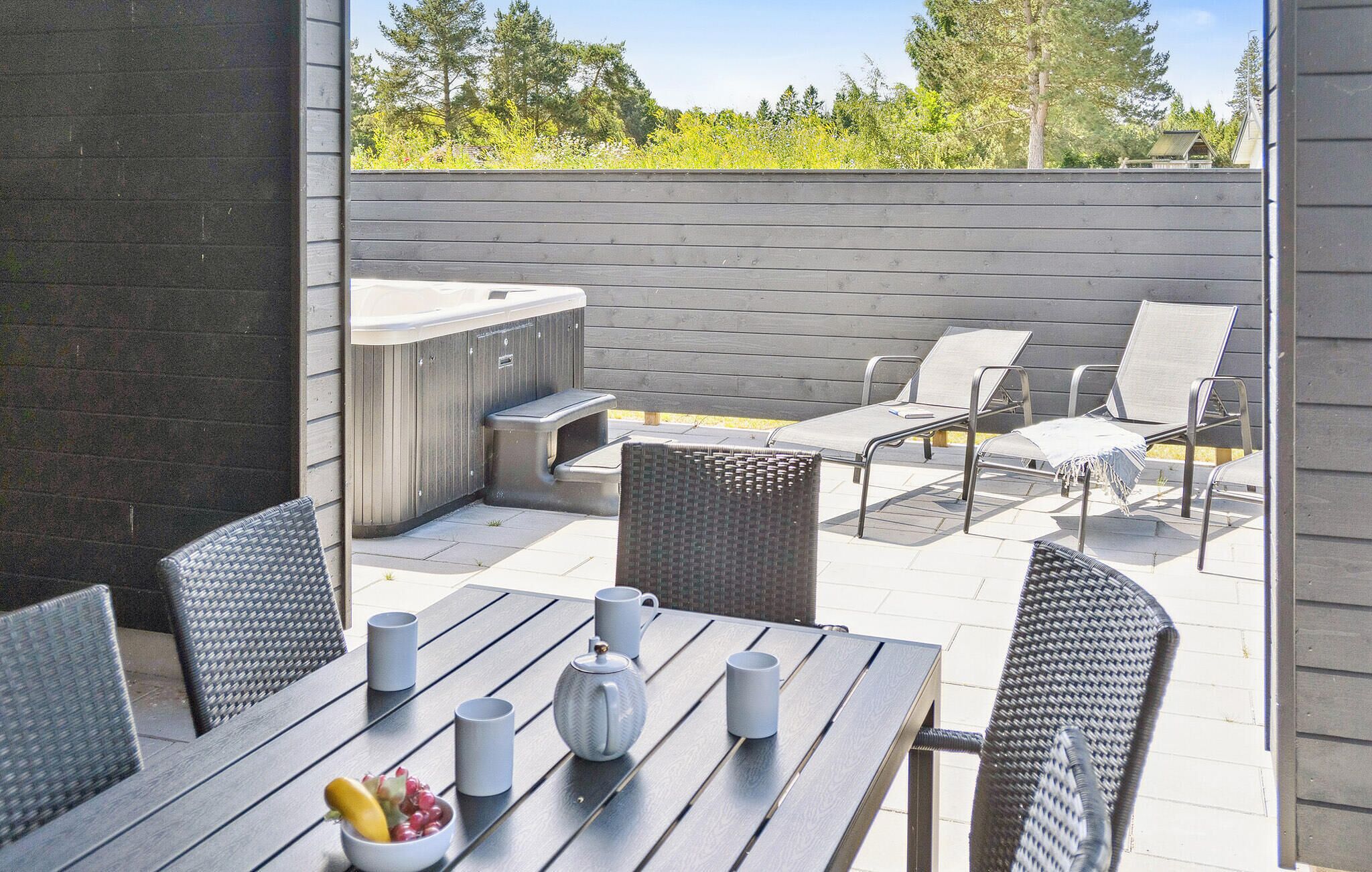 Una terrazza esterna con tavolo in legno, sedie in vimini, una vasca idromassaggio e un barbecue.