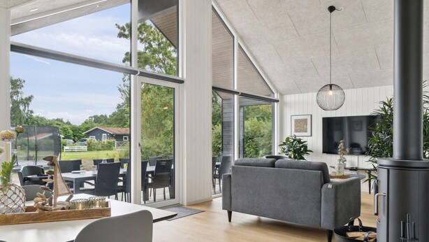 Un salon moderne doté de grandes fenêtres, d’un canapé gris, d’un coin repas et d’une cuisine équipée d’une cuisinière.