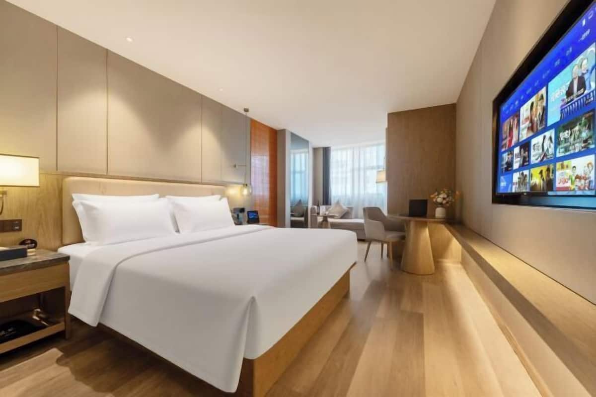 Una habitación de hotel moderna con una cama grande, un televisor de pantalla plana, un escritorio y un área de descanso.