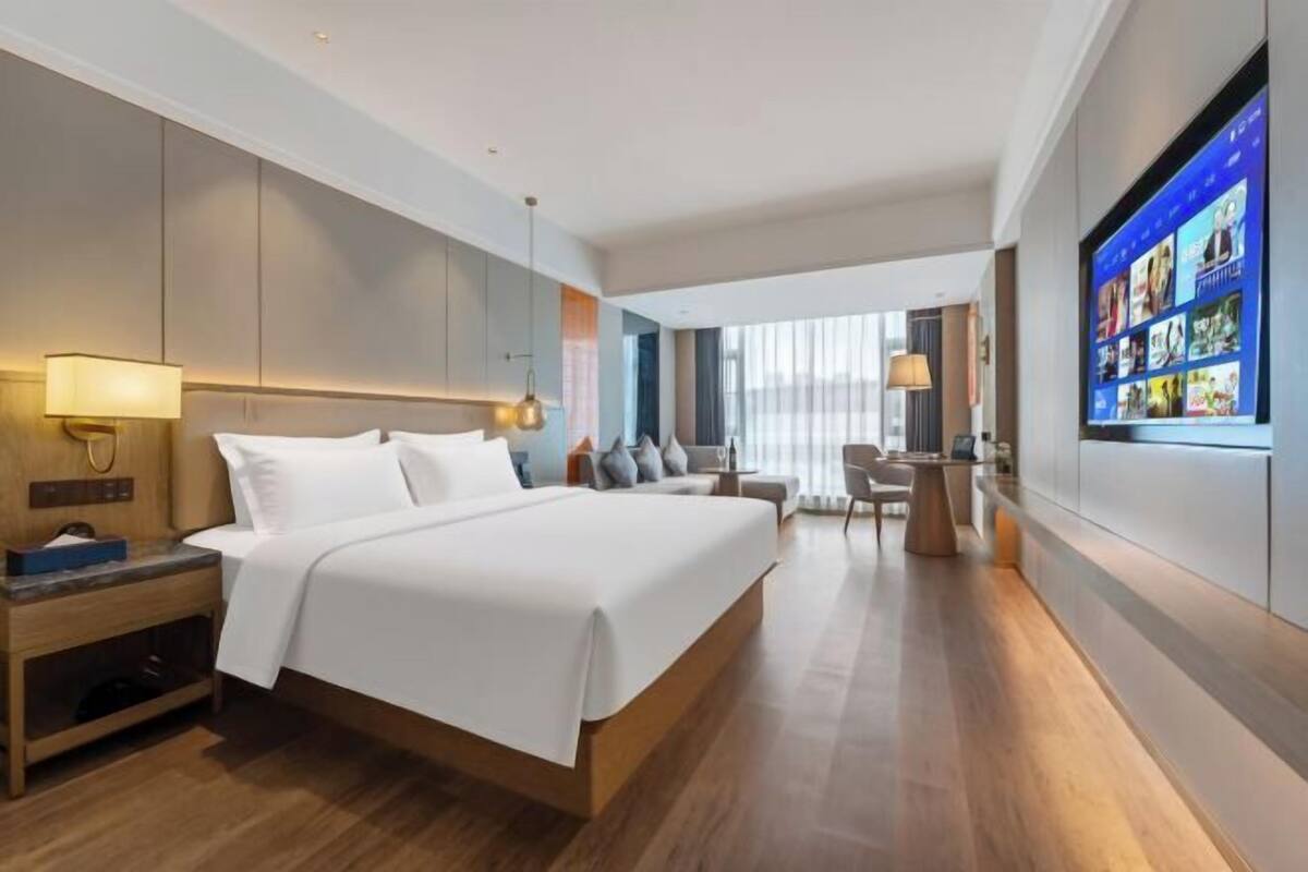 Una habitación de hotel moderna con una cama grande, mesitas de noche, una zona de estar y un televisor en la pared.