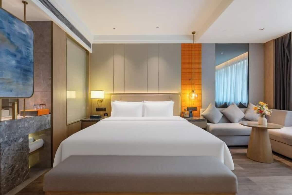 Una habitación de hotel moderna con una cama grande, un sofá, una mesita y un cuadro en la pared.
