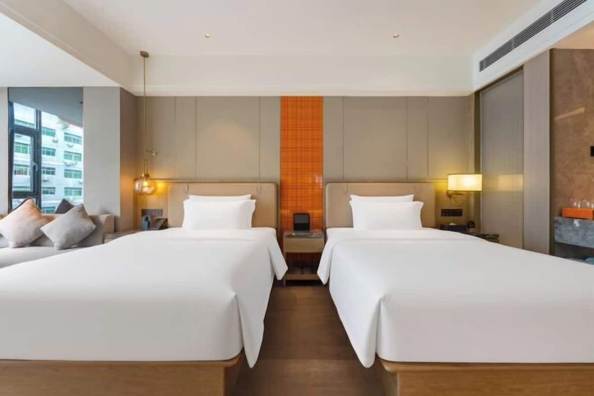 Habitación de hotel con dos camas, un sofá, una mesita de noche y vistas a la ciudad.