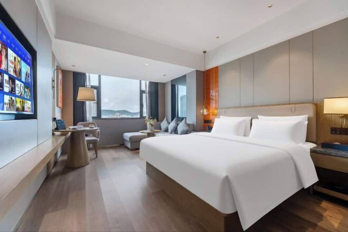 Una habitación de hotel moderna con una cama grande, un escritorio, una silla y un televisor montado en la pared.