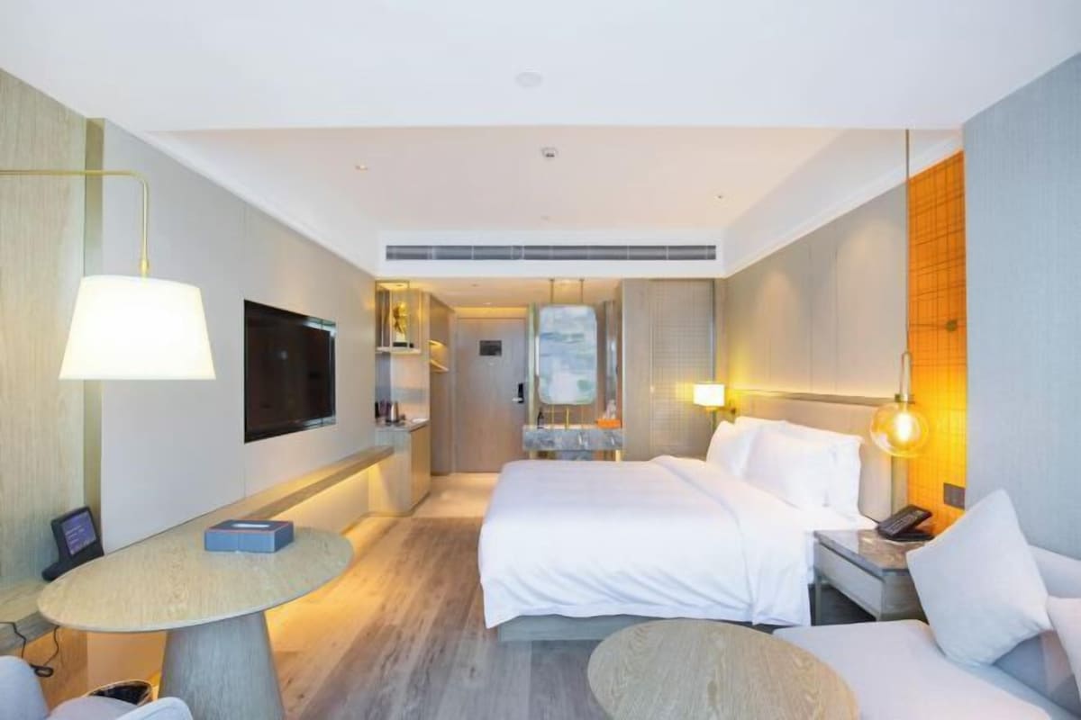 A modern hotel room with a large bed, bedside tables, a flat-screen TV, and a small round table.