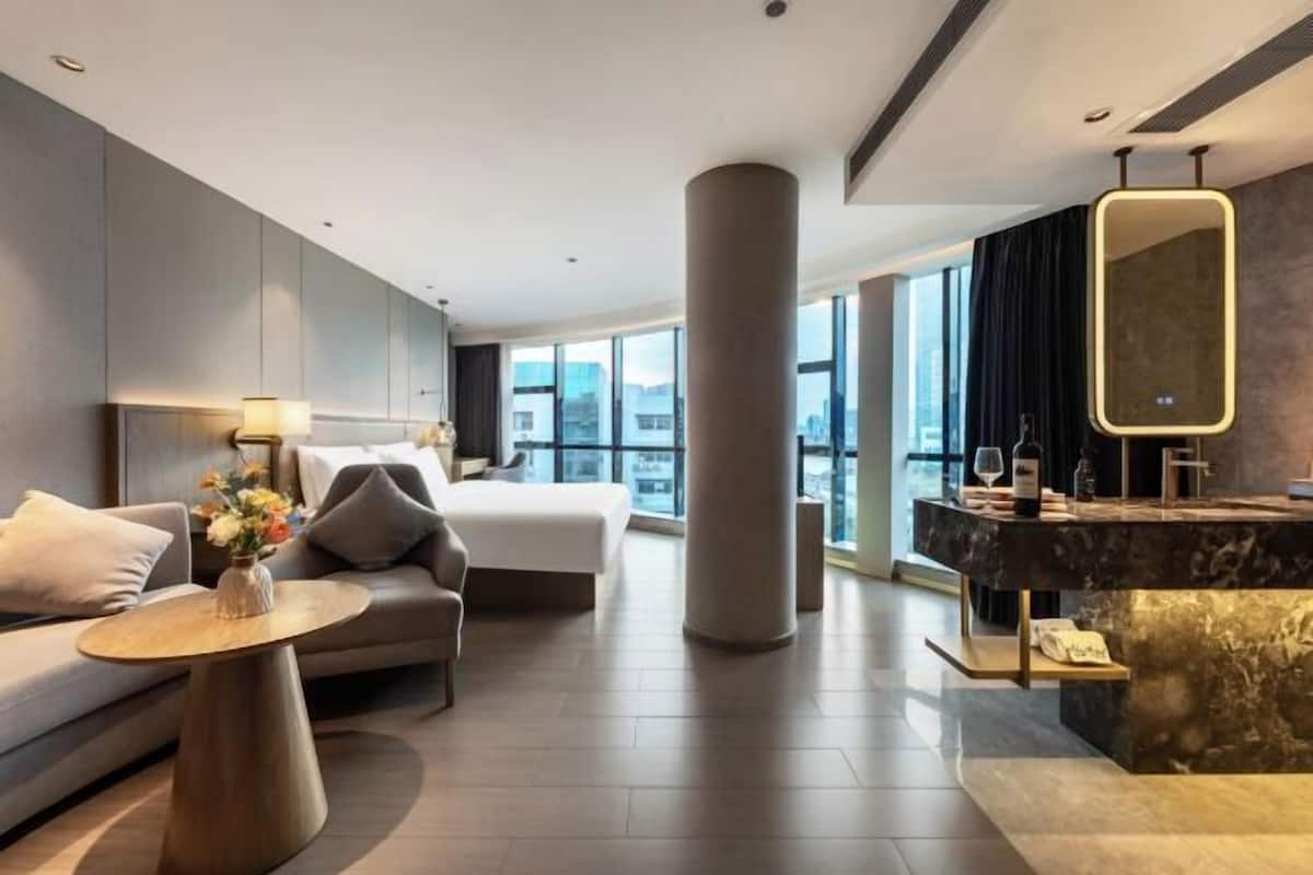 Una habitación de hotel moderna con cama, sofá, mesa redonda y tocador con espejo.