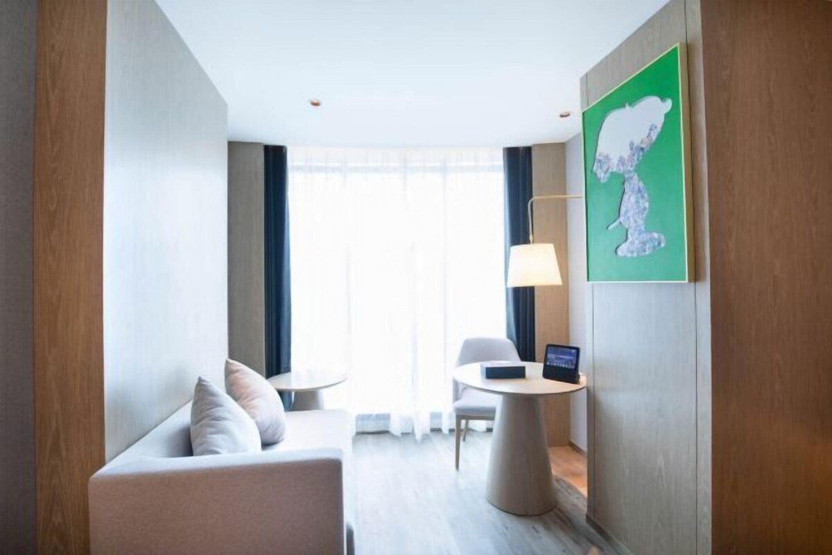 A modern hotel room with a sofa, a small round table, a lamp, and a laptop on a side table.