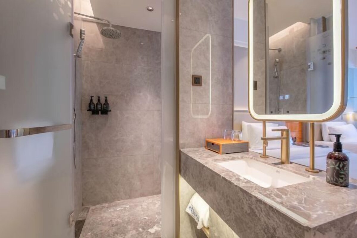 A modern bathroom with a shower, a large mirror, and a marble countertop.