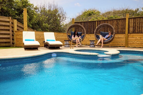 A swimming pool with lounge chairs and a wooden fence. - Casa Azul! Steps to ocean! Vilano beach! Pool, spa, oasis! Dog friendly! (St. Augustine)