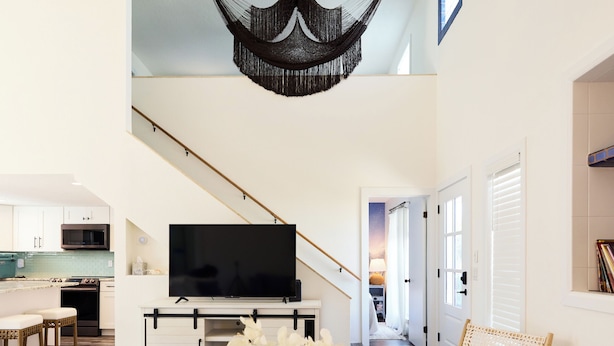Ett modernt vardagsrum med ett soffbord i glas, en vit soffa och en hängstol. En trappa leder upp till en övre våning där det finns en stor TV.