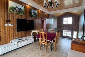 A wooden-paneled room with a TV, dining table, chairs, and a balcony with a railing. - Nantong Jinwuye Leisure Homestay (Nantong)