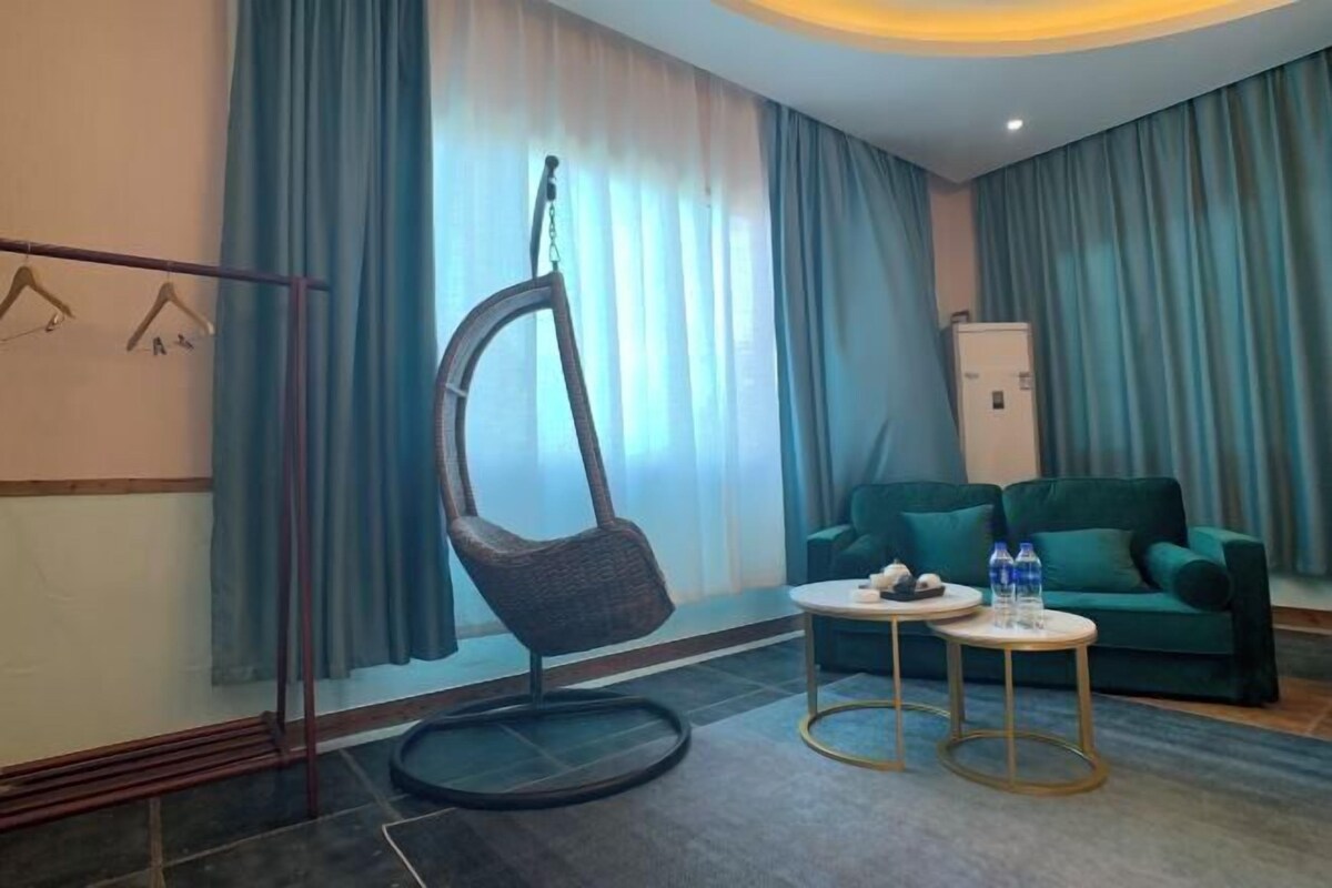 A modern hotel room with a hanging chair, a green sofa, and a small round table with water bottles.