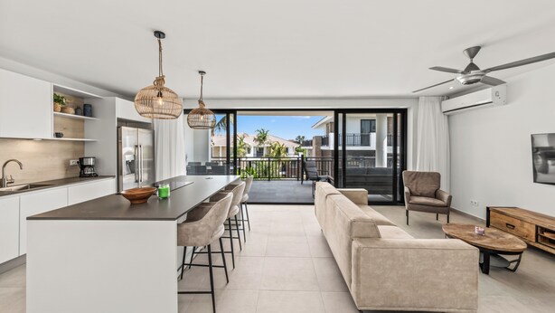 A modern kitchen with a central island, bar stools, and a dining area.